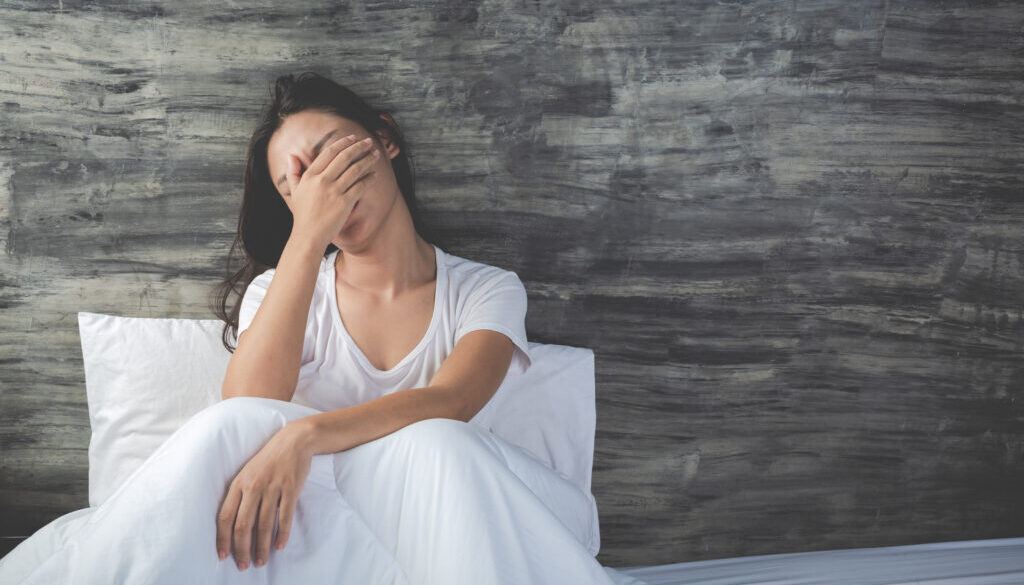 The girl is depressed on a white bed and has a gray cement wall
