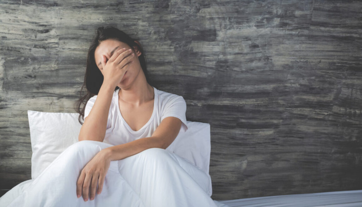 The girl is depressed on a white bed and has a gray cement wall